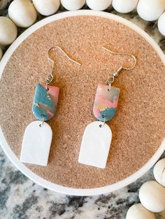 a pair of earrings sitting on top of a white plate next to some rocks and pebbles