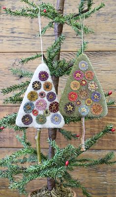 two small christmas trees are hanging on the tree branch in front of a wooden wall