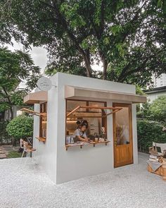 a person sitting at a table in front of a small white building with wood trimmings