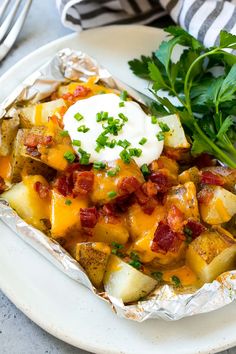 a white plate topped with potatoes covered in bacon and cheese next to a green leafy garnish