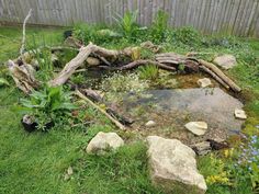 a small pond surrounded by rocks and plants in a backyard with a wooden fence behind it