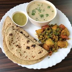 a white plate topped with food next to a bowl of soup and two tortillas