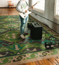 a man standing on top of a rug holding a guitar