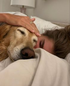 a woman laying in bed with her head on a dog's face as she sleeps