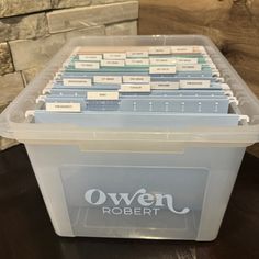 a plastic storage box filled with lots of labels on top of a wooden table next to a brick wall