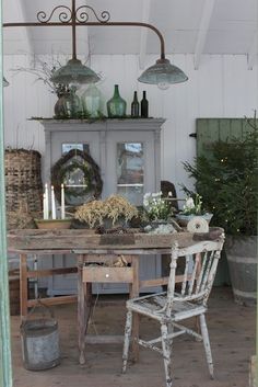 an old table and chairs are set up in the room with white walls, potted plants and candles