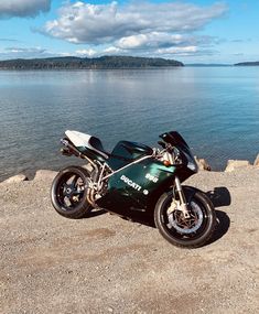 a motorcycle parked on top of a rocky beach next to the ocean with mountains in the background