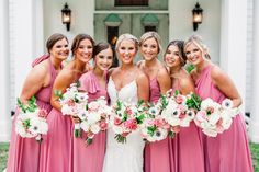 a group of women standing next to each other in front of a white building holding bouquets