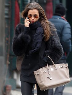 a woman is walking down the street talking on her cell phone and holding a purse