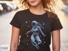 Want a space t-shirt that's out of this world? Our design features a female astronaut grooving to the cosmic beat! This comfy tee is perfect for dancers, space fans, or anyone who dreams of defying gravity. This soft and comfortable shirt lets you celebrate your love for space in style! Shop now and show off your zero-G moves! Available in a range of sizes, grab yours today and show the universe you dance to the beat of your own drum (or spacesuit!).      ♥ FIBER COMPOSITION ♥ Solid colors are 1 Space-themed Cotton T-shirt With Graphic Print, Space-themed Graphic Print Cotton T-shirt, Space-themed Graphic Crew Neck Tops, Space-themed Short Sleeve Top With Graphic Print, Space-themed Graphic Print Short Sleeve Tops, Black Cotton Space-themed T-shirt, Black Cotton T-shirt With Space Theme, Space-themed Short Sleeve Screen Print Top, Space-themed Screen Print Short Sleeve Top