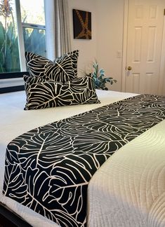 a bed with black and white comforters in front of a large window, next to a potted plant