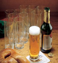 a table topped with lots of glasses filled with beer next to pretzels and a bottle