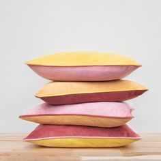 four pillows stacked on top of each other in different colors and sizes, one is pink, the other is yellow