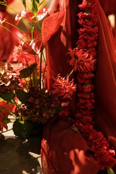 red flowers and greenery are arranged on the ground in front of an orange cloth