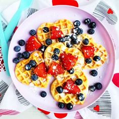 a white plate topped with waffles covered in blueberries and strawberries