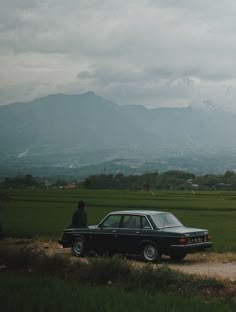 a black car parked on the side of a dirt road next to a lush green field