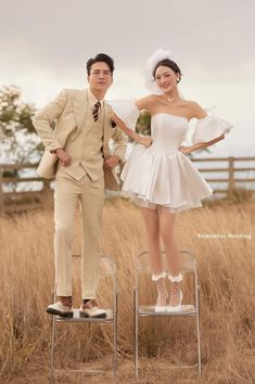 a man and woman standing on top of a chair in front of some tall grass