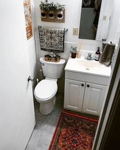 a white toilet sitting next to a sink in a bathroom under a mirror and rug