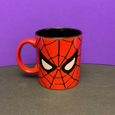 a spider - man mug sits on a table in front of a purple wall with eyes