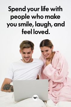 a man and woman sitting next to each other on a bed looking at a laptop