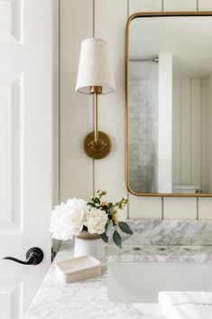 a bathroom with marble counter top and gold mirror on the wall, white flowers in vase next to sink