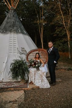 a bride and groom standing in front of a teepee