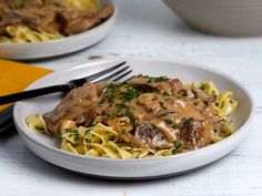 a white plate topped with pasta covered in gravy next to a bowl of meat