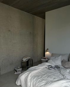 an unmade bed with white sheets and pillows in a room that has concrete walls