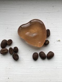 some coffee beans and a spoon on a white surface with brown liquid in the shape of a heart