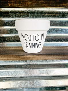 a white cup with the words mojito in training on it sitting on a wooden bench