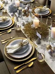 a table set for christmas with silver and gold plates, napkins, candles and decorations