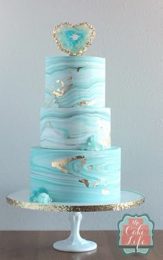 a three tiered blue cake with gold decorations on it's top and bottom