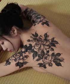 a woman laying on top of a bed next to a cell phone and flowers tattooed on her back