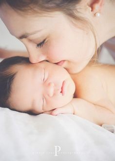 a woman holding a baby in her arms and kissing it's face with the other hand