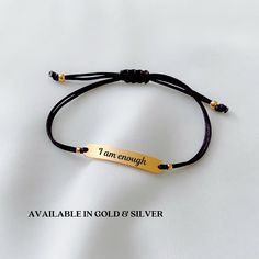 a bracelet with the words i am enough engraved in gold and silver on black cord