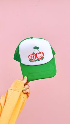 a person holding up a green and white hat with the word kaybee on it