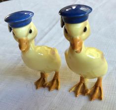 two yellow ducks wearing blue hats on top of a white cloth covered tablecloth with a wooden chair in the background