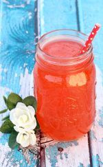 a drink with a straw in it sitting next to a flower on a wooden table