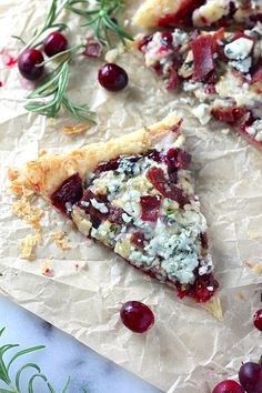 two slices of pizza with cranberry sauce and goat cheese on parchment paper next to rosemary sprigs