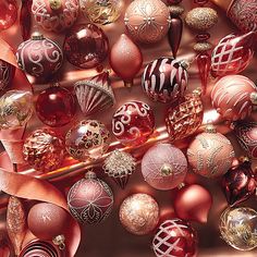 an assortment of christmas ornaments are arranged on a table with red and gold ribbons around them