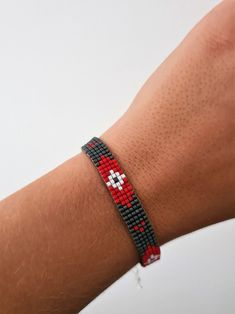 a person wearing a red and black beaded bracelet on their arm with a cross