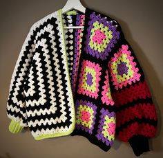 two crocheted sweaters are hanging on a hanger next to each other