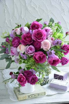 a vase filled with purple and pink flowers on top of a white table next to a stack of books