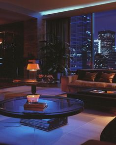 a living room filled with furniture and tall buildings in the background at night, lit up by blue lights