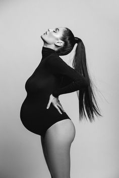 black and white photo of pregnant woman in tight bodysuit posing with her hands on her hips