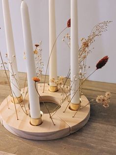 some white candles are sitting on a wooden stand with flowers in the middle and one is surrounded by smaller ones