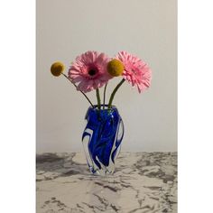 three pink flowers in a blue vase on a marble countertop with white walls behind it