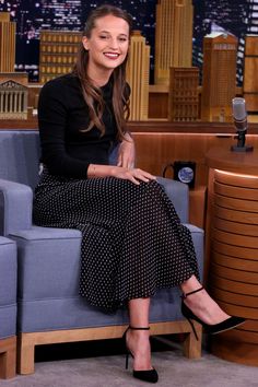 a woman sitting on top of a blue couch in front of a microphone and wearing black heels