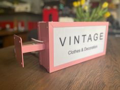 a pink sign sitting on top of a wooden table next to a vase with flowers