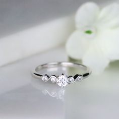 a white flower sitting on top of a table next to a ring with three stones